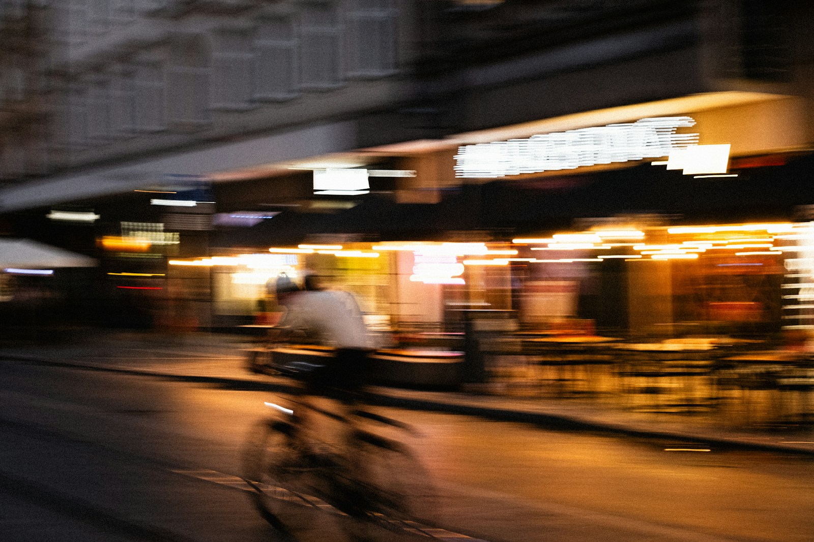 Photo by Maksim Samuilionak Blurred cyclist rides past illuminated storefronts at night
